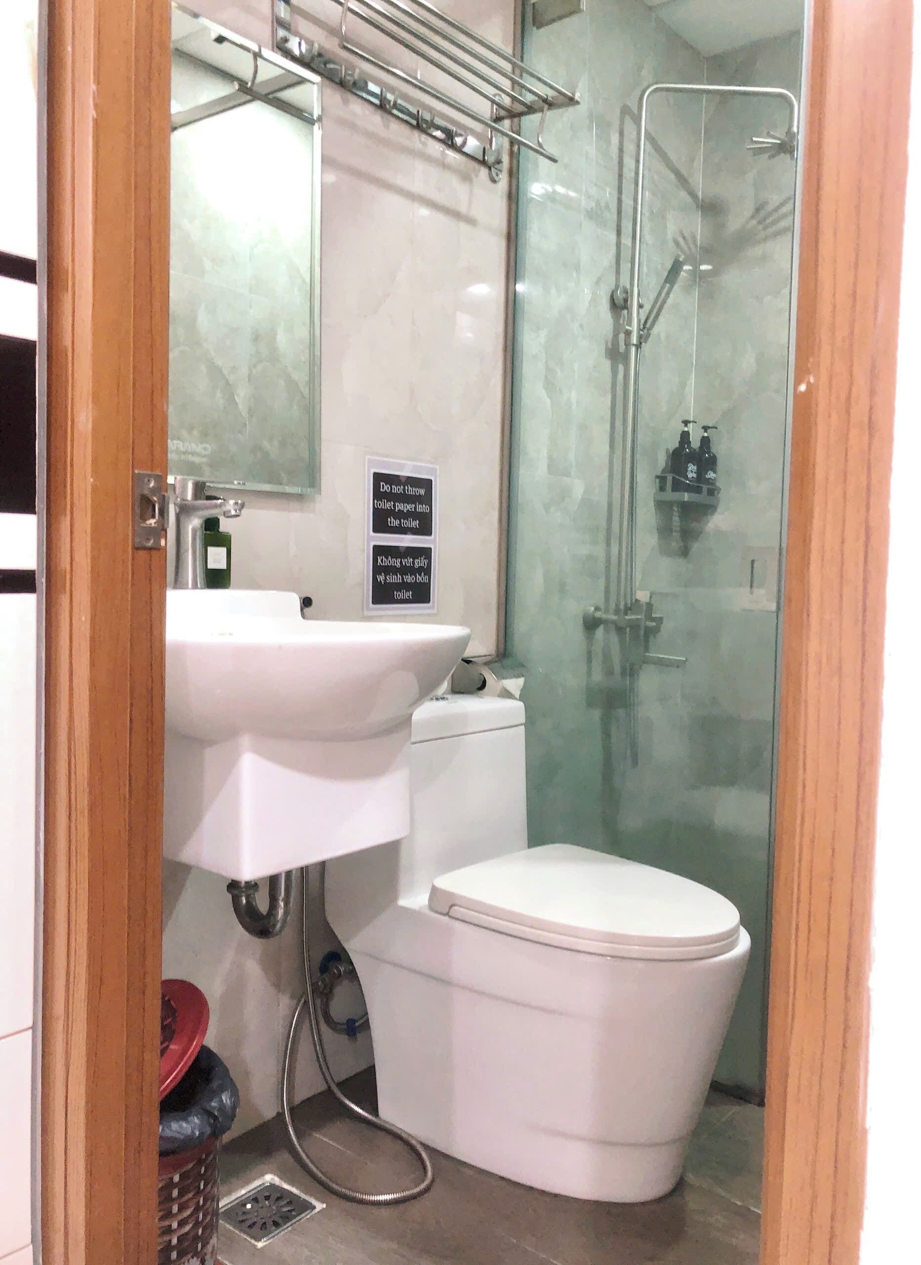 Ein Badezimmer mit weißem Waschbecken, WC und einer Duschkabine. Ein Schild weist darauf hin, kein Toilettenpapier in die Toilette zu werfen.