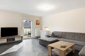 A living room with a TV, sofa, coffee table, and a door leading outside.