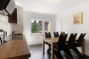 A modern kitchen with a wooden table and chairs, a window with a view of houses, and a framed picture on the wall.
