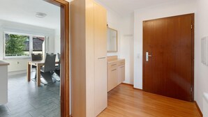 Quarto com porta de madeira, uma pequena mesa com cadeiras e janela com persianas.