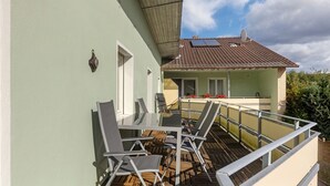 Uma varanda com mesa e cadeiras, um corrimão e um edifício com telhado em azulejos e janelas.