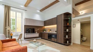Een moderne woonkamer met een bank, salontafel en televisie. Er is een keukenhoek met kasten en een eettafel.