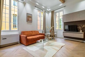 A modern living room with a sofa, a glass coffee table, a TV, and a fireplace.