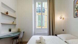 Hotelkamer met een bed, een bureau, een stoel, een raam met luiken en een wandlamp.