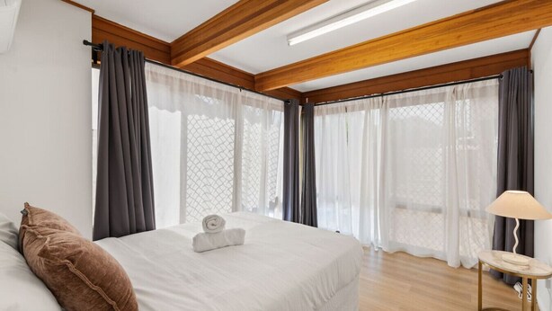 A hotel room with a large bed, a small round table, and a lamp. - Modern 3-Bedroom Stay | Walk to Shops & Dining (Robertson)