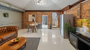 A modern living room with a leather sofa, dining table, and a TV. - Modern 3-Bedroom Stay | Walk to Shops & Dining (Robertson)