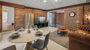 A dining area with a round table set for four, a leather couch, and a television in the background. - Modern 3-Bedroom Stay | Walk to Shops & Dining (Robertson)