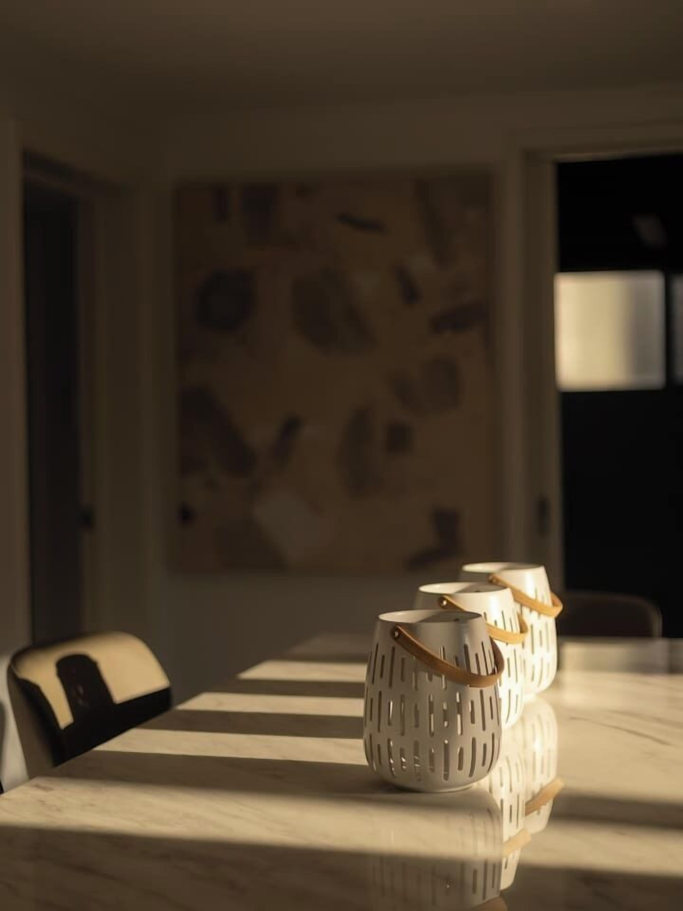 A dining table with a striped tablecloth, a chair, and three white candle holders with handles.