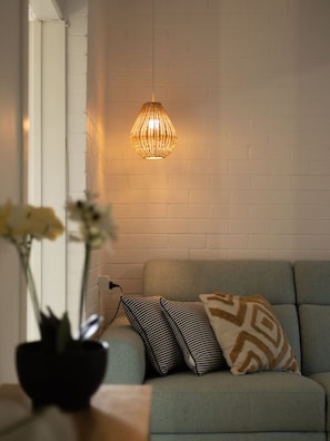 Et værelse med en sofa, en hængende lampe og en vase med blomster.