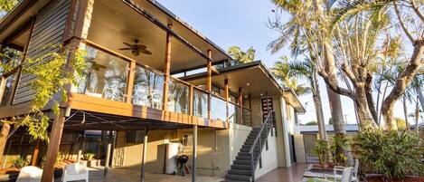 A modern two-story house with a covered patio, outdoor seating, and a staircase leading to the upper level.