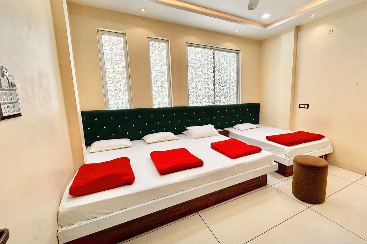 Habitación de hotel con una cama grande, dos ventanas con persianas florales, un taburete pequeño y piso de baldosas.