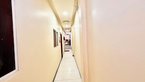Un couloir étroit et bien éclairé, aux murs blancs et au sol carrelé, qui mène à une pièce située au fond.