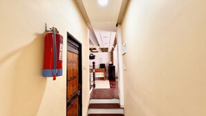 Un couloir étroit, avec un extincteur fixé au mur, une porte en bois portant l’inscription « ALDURA » et un escalier menant à une pièce où se trouvent un bureau et une chaise.
