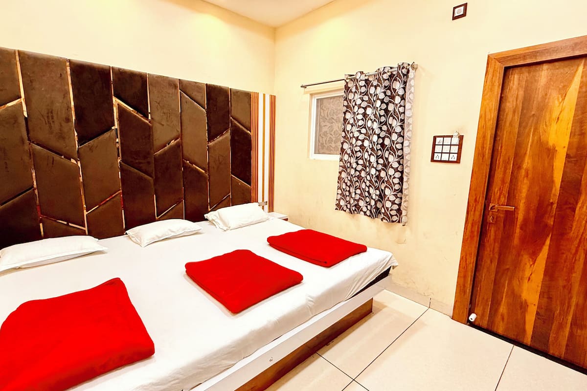Una habitación de hotel con una cama grande, una puerta de madera y un ventanal con cortinas estampadas.