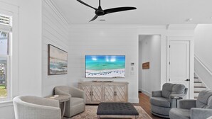 Un salon comprenant un téléviseur, deux fauteuils, un canapé, un ventilateur de plafond et un meuble en bois.