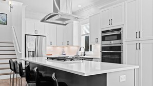 Une cuisine moderne avec des meubles blancs, un réfrigérateur en acier inoxydable, deux fours et un îlot central doté de tabourets de bar.