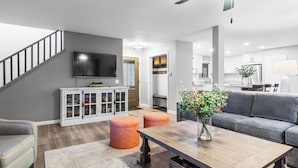 Una sala moderna con una escalera, un televisor de pantalla plana, un comedor y una cocina al fondo.