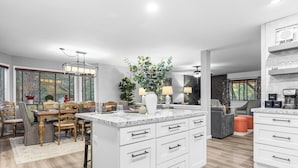 Una cocina moderna con armarios blancos, una isla central y un comedor con sillas y una mesa de madera.