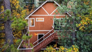 Una cabaña de madera con escaleras, rodeada de árboles y follaje otoñal.