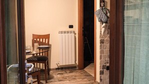 Un pasillo estrecho con suelo de piedra, una puerta de madera, un radiador y una silla.