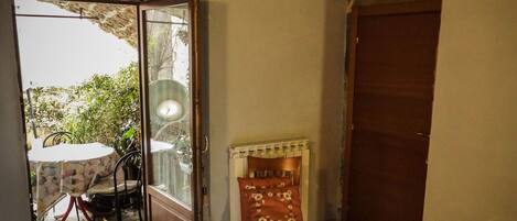 Un dormitorio con cama, una silla, una mesita y una puerta que da a un área exterior con mesa y sillas.