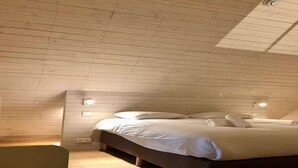 A bedroom with a wooden sloped ceiling, a bed with white bedding, and two wall-mounted lights.
