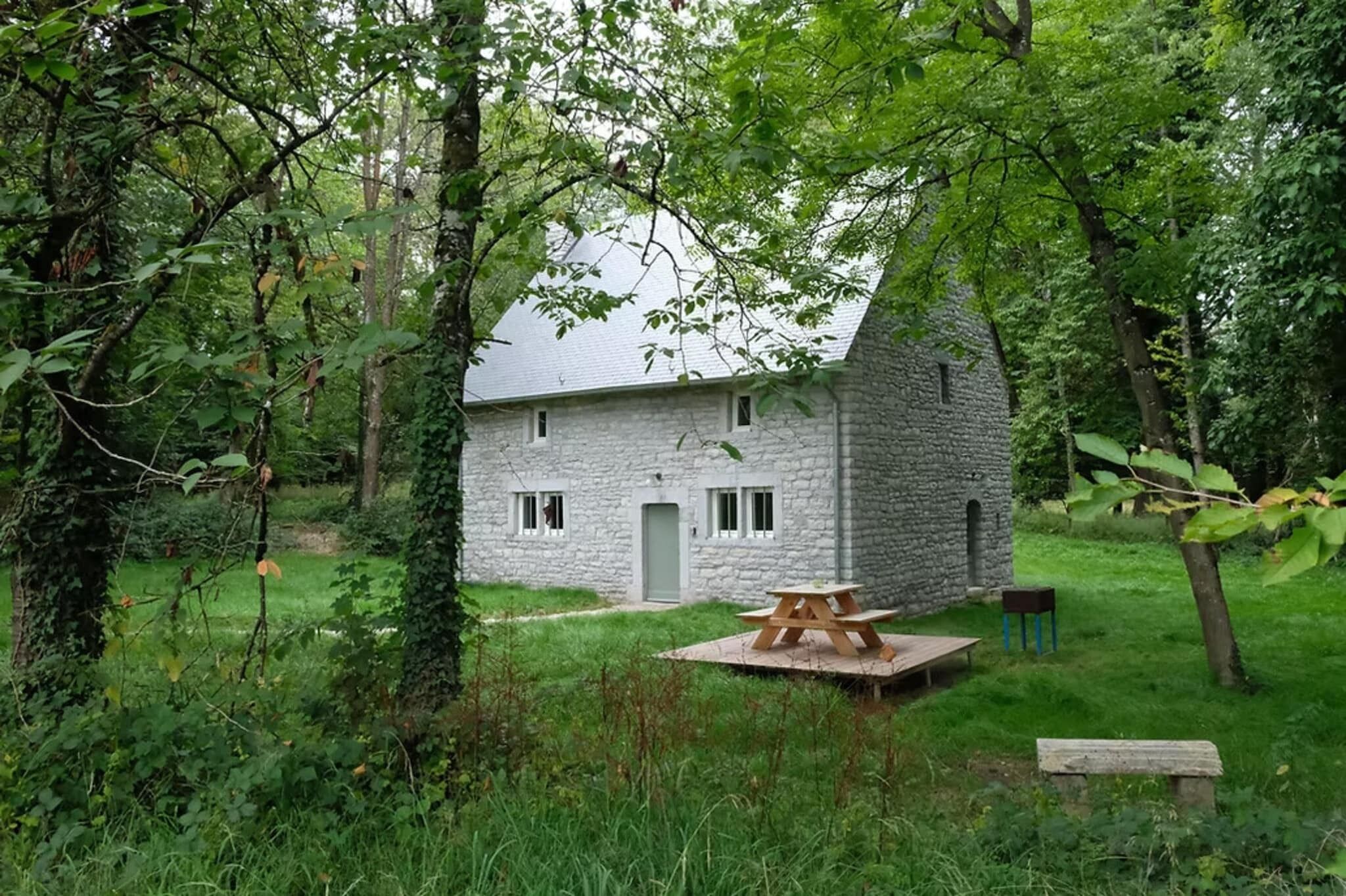 Een stenen cottage met een kleine tuin, een picknicktafel en een houten bank.