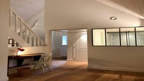A room with a wooden floor, a desk with a lamp, a chair, and a window with blinds.