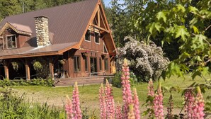 Une cabane rustique dotée d’une cheminée en pierre, de poutres en bois et d’un porche agrémenté de jardinières suspendues.