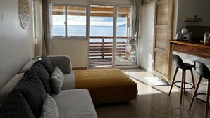A room with a sofa, a small table, and a view of the sea through a sliding door.