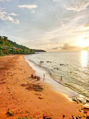 A beach with people swimming and walking along the shore, a clear sky, and a sunset. - T2 cosy Côte îlots au bord de la plage vue panoramique, coucher de soleil. (Canton d'Acoua)