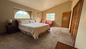 A bedroom with a large bed, two windows, a wooden wardrobe, and a red chair. - Family Friendly 3-bedroom house in lovely Three Rivers with AC (Three Rivers)