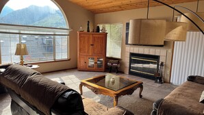 A cozy living room with a fireplace, wooden furniture, and a large window offering a mountain view. - Family Friendly 3-bedroom house in lovely Three Rivers with AC (Three Rivers)