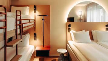 Una habitación de hotel con una cama individual superpuesta, una mesita redonda pequeña, una lámpara y un espejo.