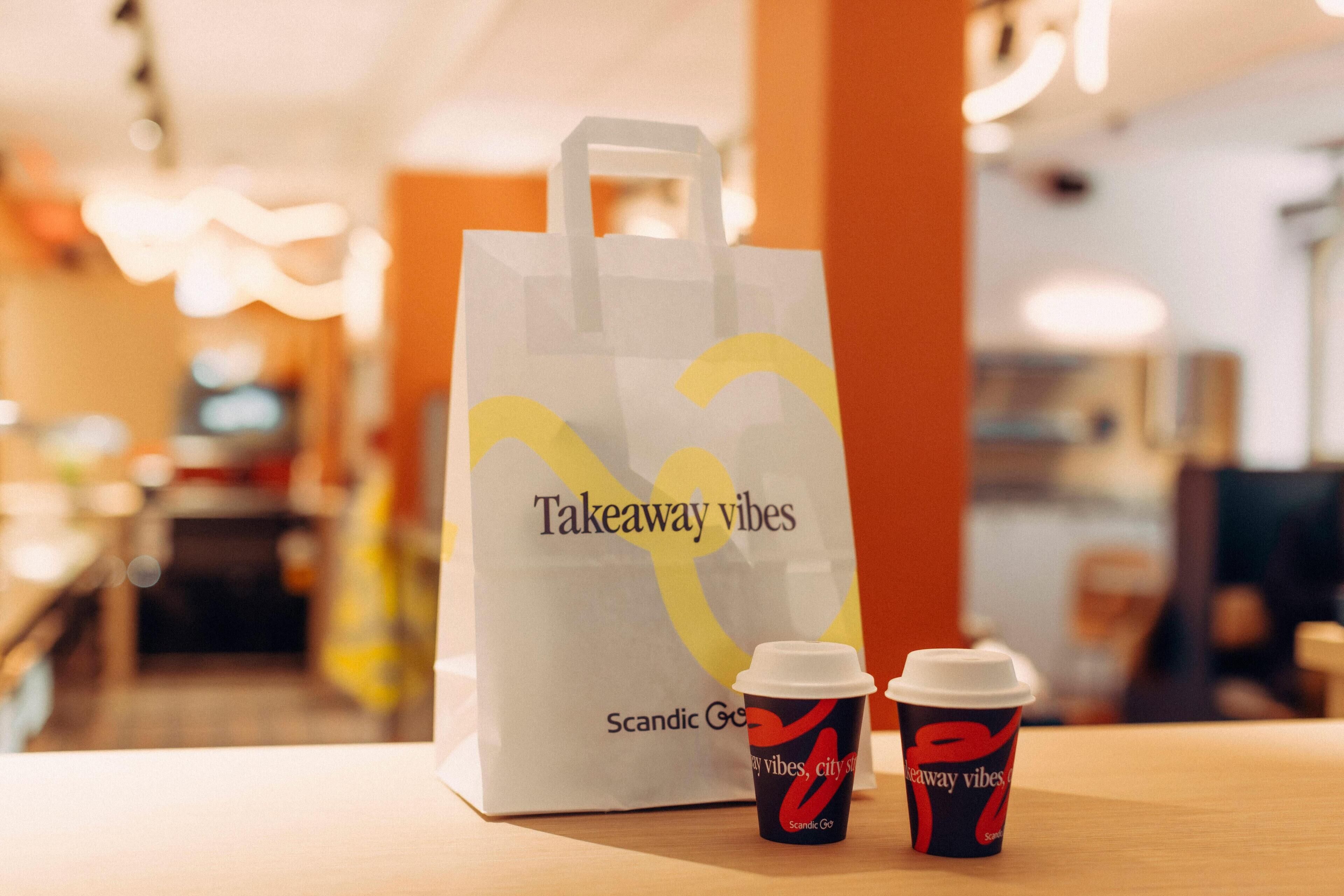 A takeaway bag and two cups on a table in a cafe.