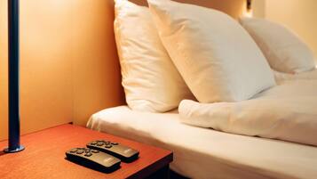 Ein Hotelzimmer mit einem Bett, Kissen, einem Nachttisch mit Fernbedienung und einer Wandlampe.