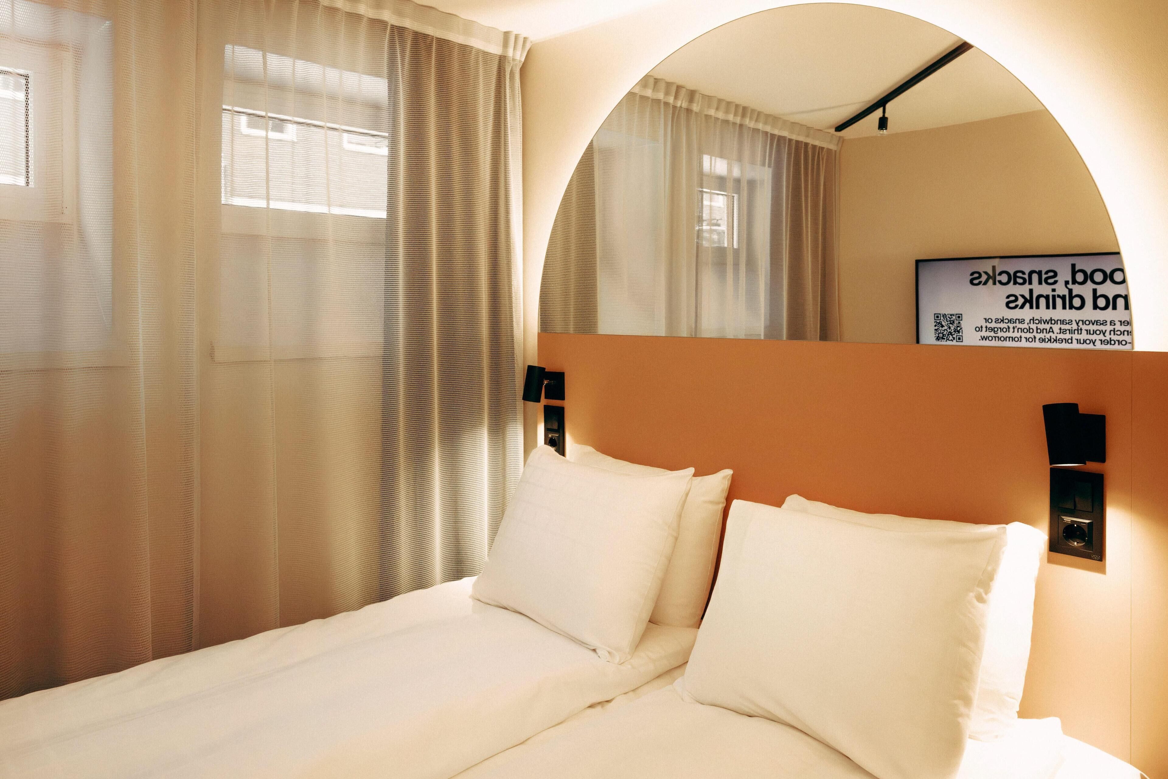 A hotel room with a bed, curtains, a mirror, and a sign on the wall.