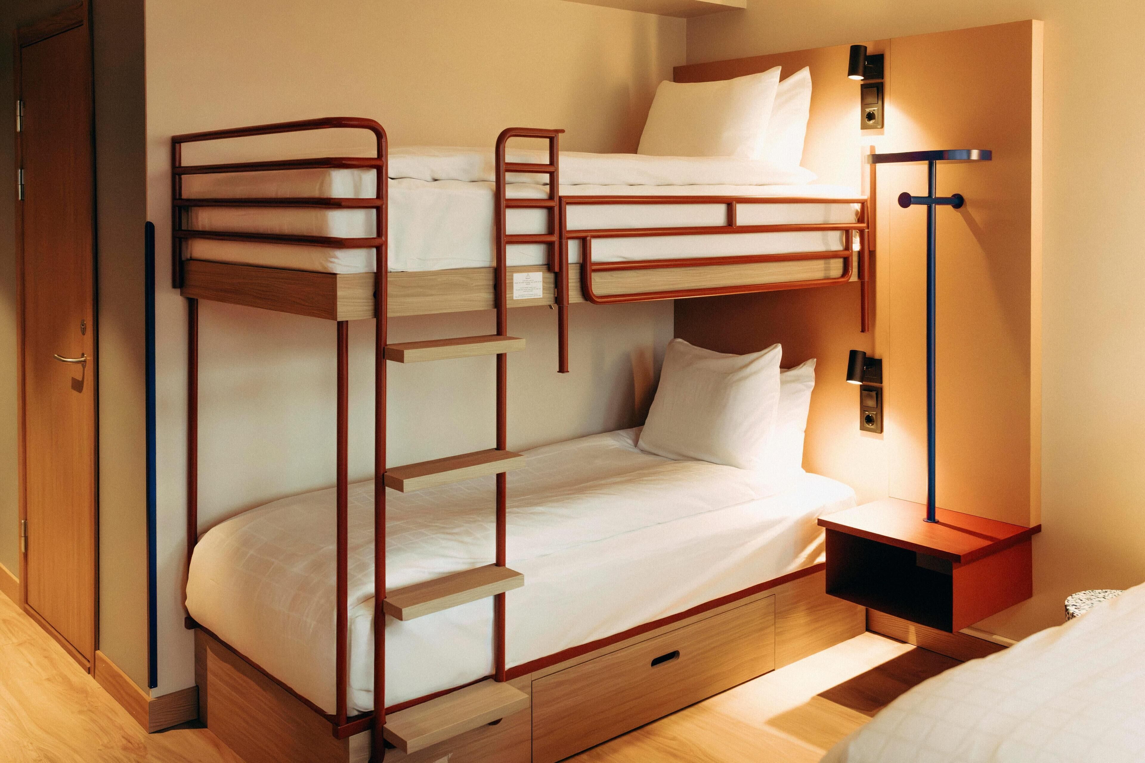 A bunk bed room with a wooden ladder, a bedside table with a lamp, and a wardrobe.