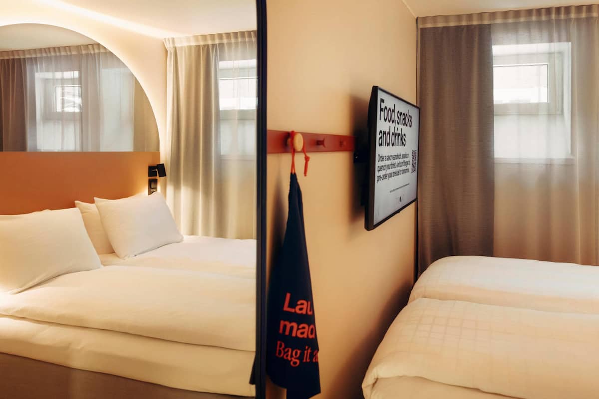 A hotel room with two beds, a wall-mounted TV, and a sign offering food, snacks, and drinks.