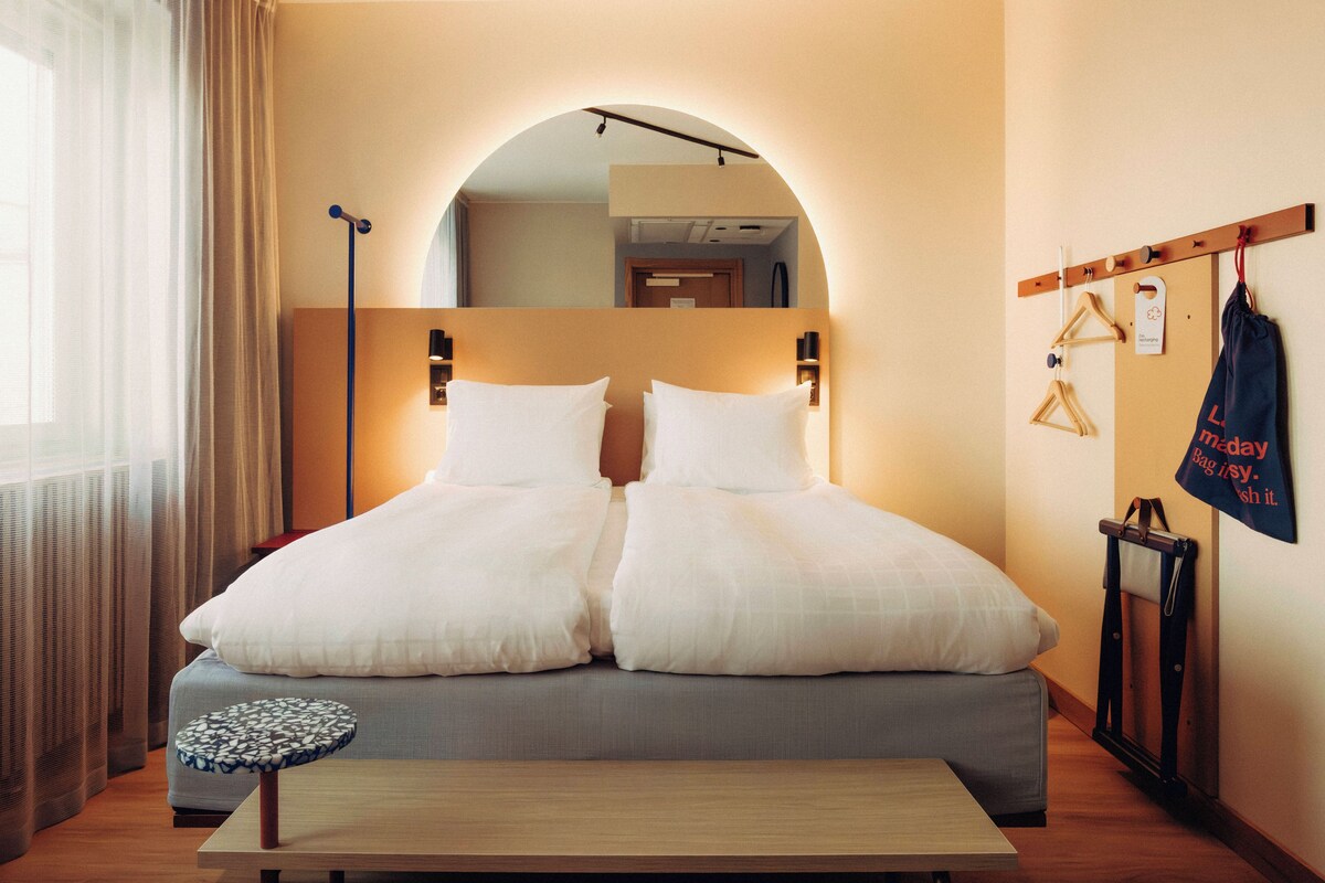 A double bed with a headboard, a bedside table, and a hanging bag rack.