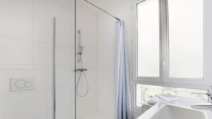 A modern bathroom with a glass shower enclosure, a window with a view, and a white sink.