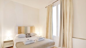 A neatly made bed with white linens and a beige throw blanket, a bedside lamp, and a wooden headboard.