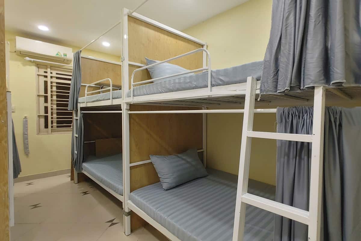 A dormitory room with bunk beds, a window with bars, and a curtain.