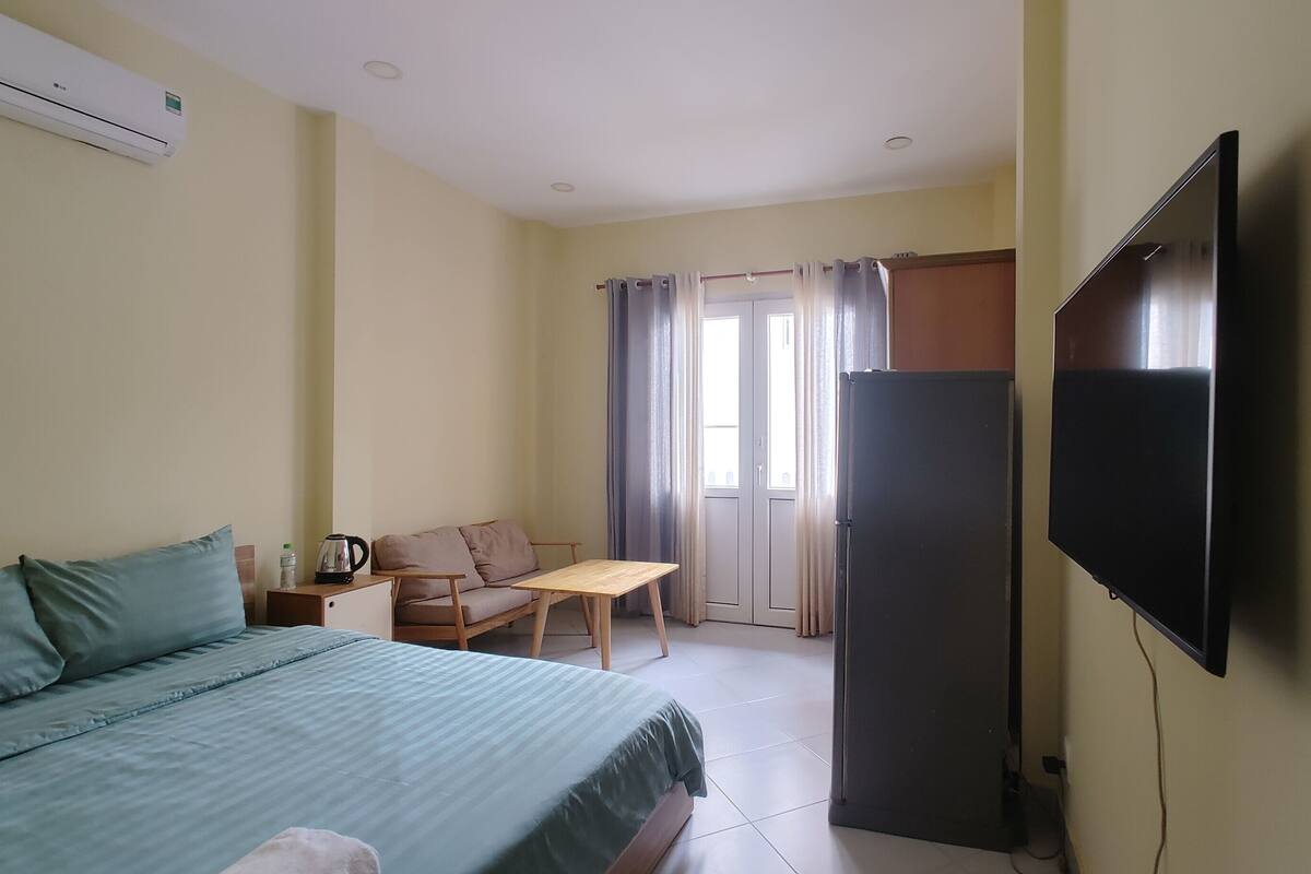 A bedroom with a bed, a desk, a chair, a television, and a refrigerator.