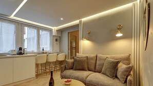 Ein modernes Wohnzimmer mit einer Couch, einem Couchtisch mit Flasche und Gläsern sowie einer Küchenzeile mit Barhocker.