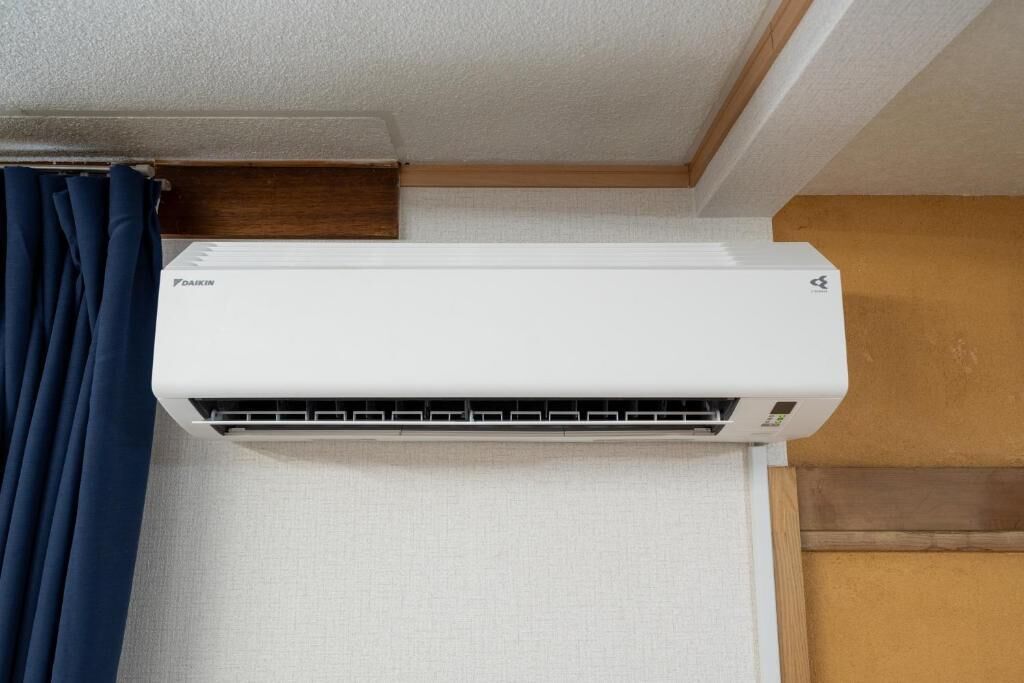 A white Daikin air conditioner mounted on a wall with a wooden trim and a white curtain.
