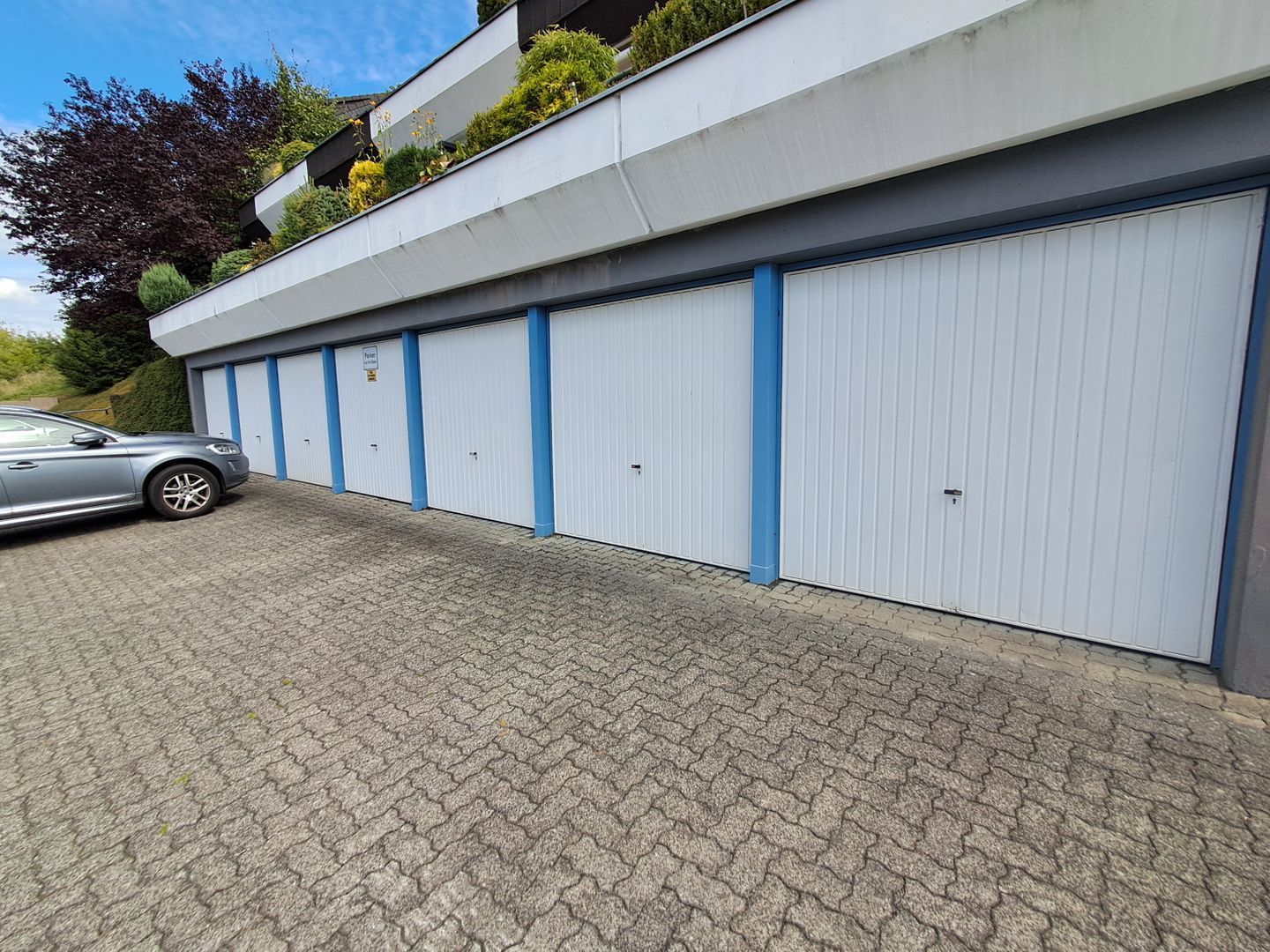 A building with multiple garage doors, a paved driveway, and a parked car.