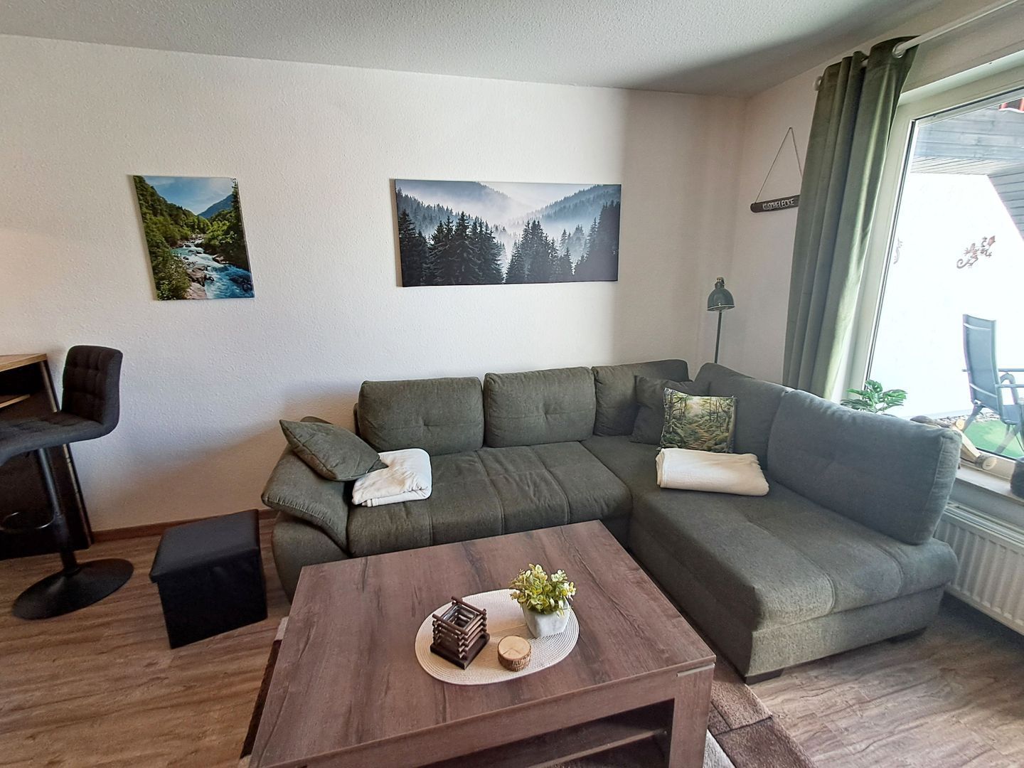 A modern living room with a sectional sofa, a small table with decorative items, and two landscape paintings on the wall.