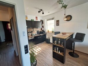 Eine moderne Küche mit dunklen Schränken, einer Holz Arbeitsplatte und einem eingebauten Ofen. Es gibt einen Essbereich mit einem Holztisch und schwarzen Stühlen.