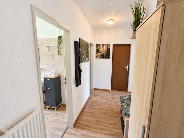 A hallway with a wooden floor, a door, a cabinet, and a plant.
